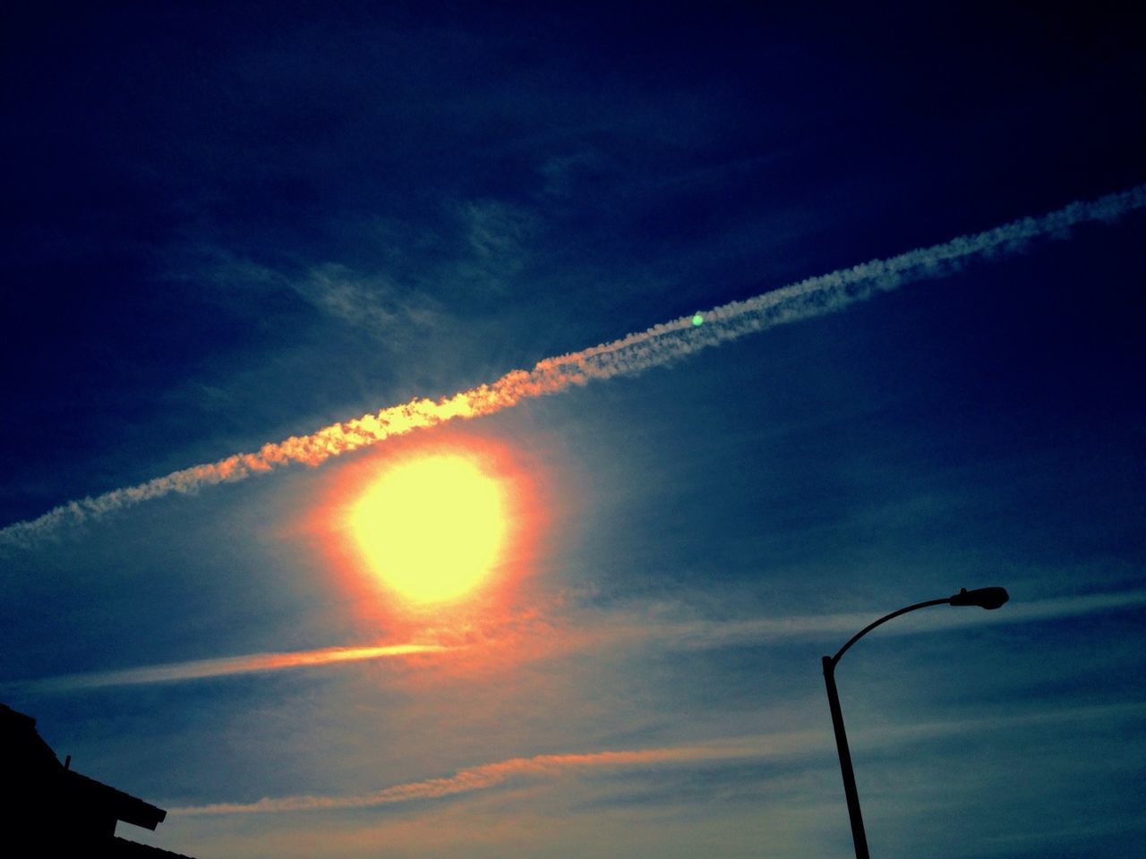 sky, low angle view, sunset, cloud - sky, silhouette, sun, street light, beauty in nature, blue, scenics, nature, vapor trail, tranquility, cloud, sunlight, sunbeam, outdoors, tranquil scene, no people, lighting equipment