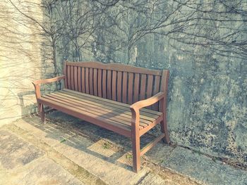 Empty bench in park against wall