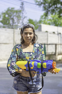 Portrait of smiling young woman holding squirt gun on road