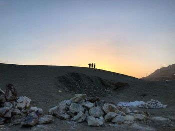 Silhouette people standing at desert against clear sky during sunset