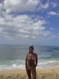 Beautiful woman wearing bikini standing on beach against sky