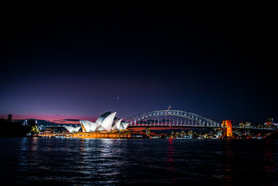 Illuminated bridge over river against sky at night