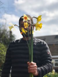 Low angle view of man holding yellow flowers against cloudy sky