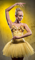 Beautiful ballerina dancing against wall in dark