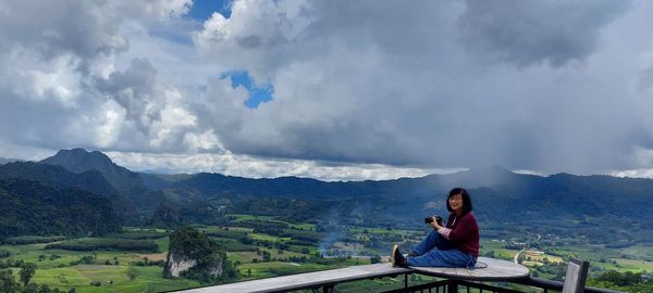 Woman sitting on mountain against sky