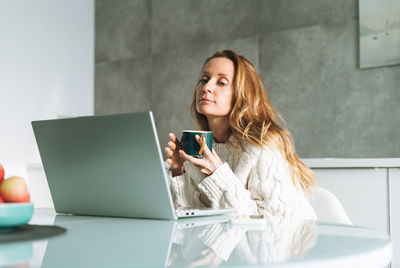 Young adult forty years blonde woman with long hair working on laptop at home, remote work