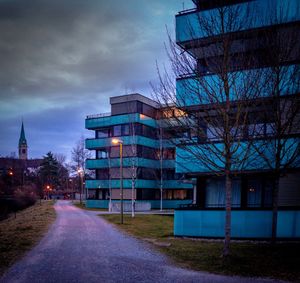 Road by buildings against sky at dusk