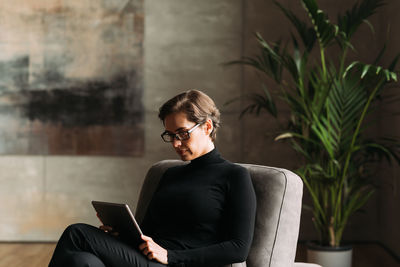 Young man using laptop while sitting against wall