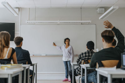 Mature female teacher pointing at whiteboard while teaching students in classroom