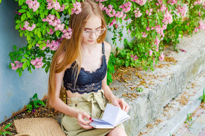 Teenage girl reading book while sitting by wall