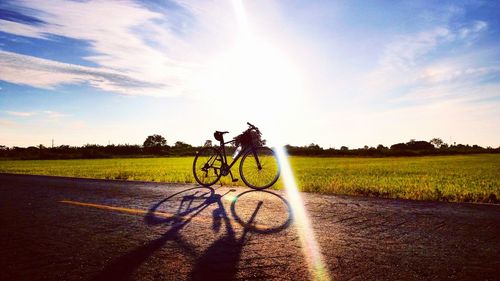 Bicycle on field by road against sky