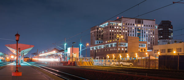 Illuminated railroad tracks in city against clear sky at night