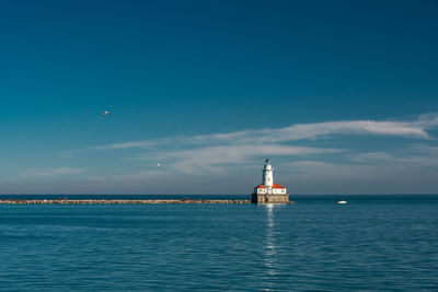 Lighthouse by sea against blue sky