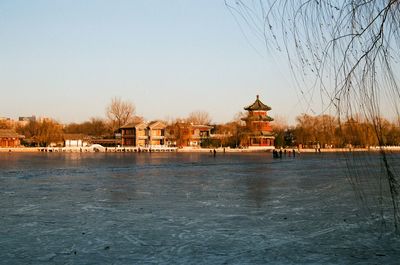 Building by river against clear sky during winter