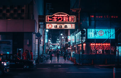 People walking on illuminated footpath in city at night