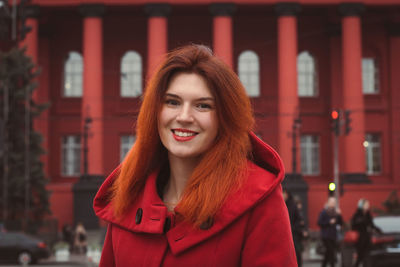 Close up young smiling woman in red coat on street portrait picture