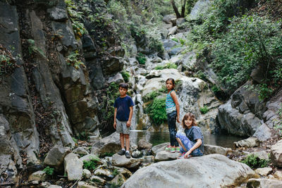 Portrait of sisters on rocks with brother by stream