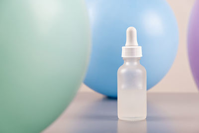 Face serum oil dropper glass bottle with pipette with colored balloons background close up