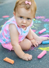 Cute baby with chalk sitting on sidewalk