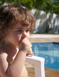 Baby girl eating a banana at pool on a sunny day.