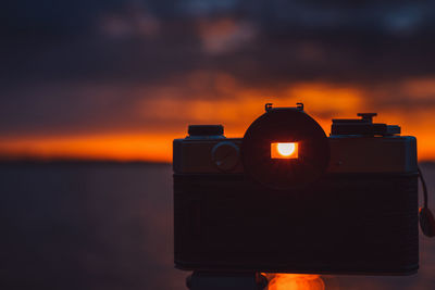 Close-up of illuminated camera against sea during sunset