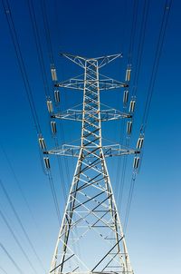 Low angle view of electricity pylon against clear blue sky