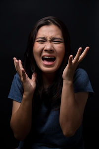 Scared young woman screaming while standing against black background