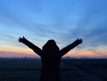 Silhouette woman with arms raised on field against sky during sunset
