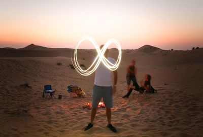 Blurred motion of man light painting at desert against sky during sunset