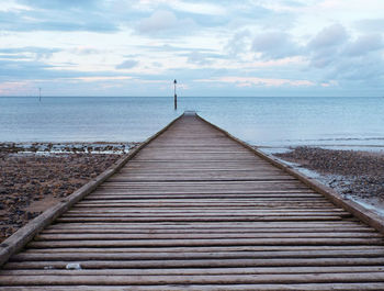 Boardwalk leading towards sea against sky