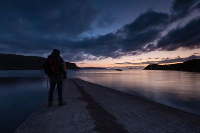 Rear view of man standing on lake against sky during sunset