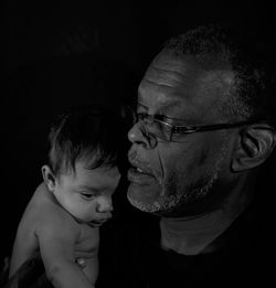 Close-up of father carrying baby boy against black background
