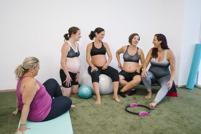 Group of pregnant females laughing while doing exercise at yoga studio