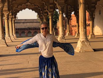 Portrait of woman with arms outstretched standing at historic building