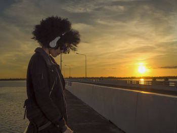 Side view of woman standing on beach against sky during sunset