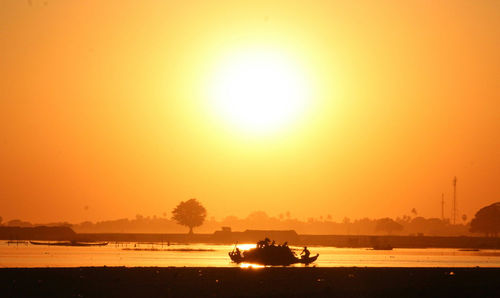 Silhouette people on sea against orange sky