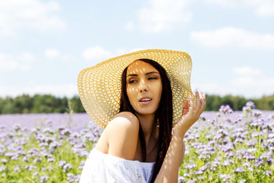 Young woman wearing hat while standing amidst plants against sky