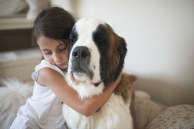 Girl embracing saint bernard while sitting on bed at home