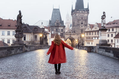 Rear view of woman standing on bridge against buildings in city