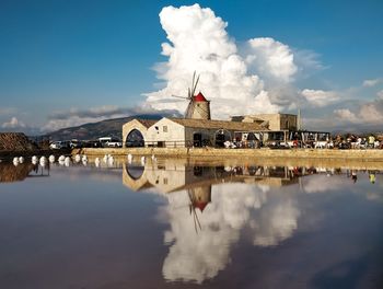 Traditional windmill by lake against cloudy sky