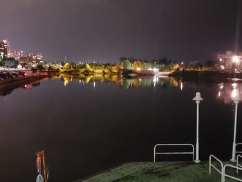 Illuminated buildings by river against sky at night