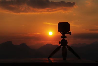 Silhouette camera against mountains during sunset