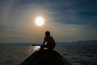 Rear view of man on sea against sky during sunset