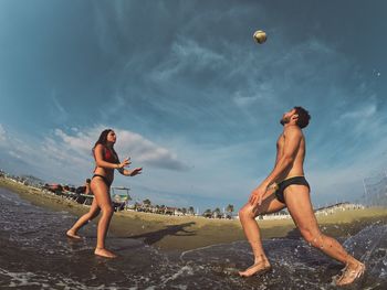 Full length of shirtless man and woman playing at beach against sky