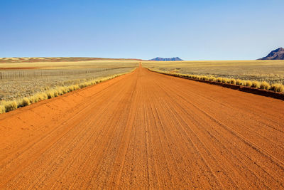 Tire tracks on agricultural field against clear blue sky