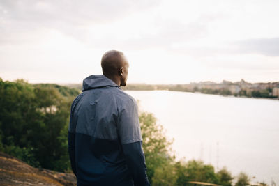 Male athlete looking at sea while standing on hill against sky