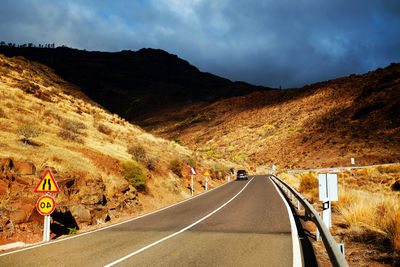 Diminishing perspective of road passing through mountains against cloudy sky