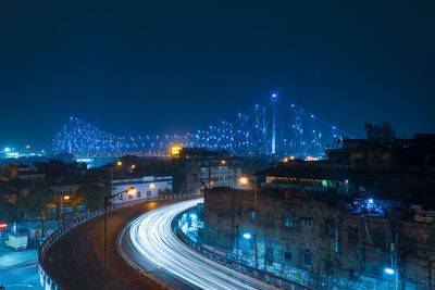 Illuminated street amidst buildings against blue sky at night