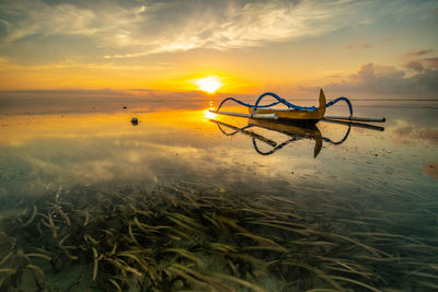 Outrigger boat on sea against sky during sunset