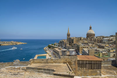 Buildings by sea against clear sky